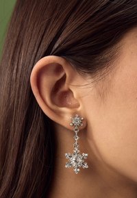 Srebrne naušnice u obliku pahuljica s detaljima od kristala i visećim dizajnom, prikazujući mješavinu oblika i tekstura.