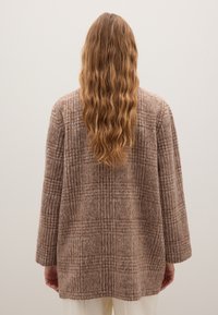 Brauner kariierter langer Mantel mit lockerer Passform, aus strukturiertem Stoff. Verfügt über einen geraden Schnitt, lange Ärmel und einen Reverskragen.
