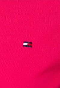 Rosa Baumwollstoff mit einem strukturierten Muster. Enthält ein kleines gesticktes Logo mit rot-weißen und blauen Streifen.