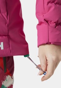 Dettaglio della manica di una giacca a vento rosa con elastico e cordino multicolore. Il tessuto ha una texture liscia, con cuciture visibili.