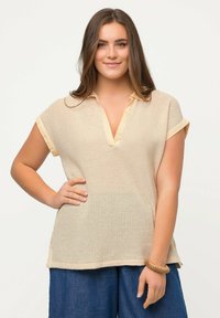 Top corto a maniche corte in maglia beige chiaro con scollo a V e orli arrotolati, caratterizzato da un motivo testurizzato e fessure laterali per facilitare i movimenti.