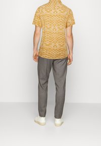 Camisa de manga corta con cuello en amarillo con un patrón geométrico, combinada con pantalones grises ajustados y zapatillas blancas. Textura de tela suave.