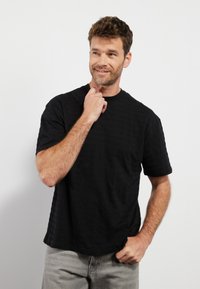 Svart kortermet t-skjorte med en strukturert stripemønster, rund halsdesign og avslappet passform. Kombinert med lyse grå jeans.