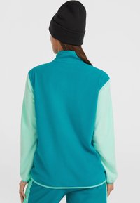 Fleece-Pullover in Türkis mit mintgrünen Ärmeln, hohem Kragen und langen Ärmeln. Weicher Stoff, figurbetonter Schnitt, keine sichtbaren Beschläge.
