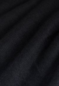 Primer plano de tela negra oscura que muestra una textura suave y de tejido apretado con pliegues y sombras suaves.