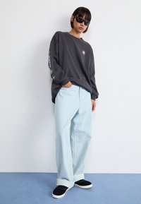Oversized antraciet sweatshirt met grafische details op de mouw, gecombineerd met lichtblauwe wijde jeans en zwarte suède sneakers.