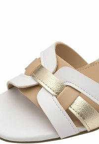 Sandalo bianco e beige con design a bande incrociate, caratterizzato da un'accenno dorato lucido. Texture liscia e stile open-toe.