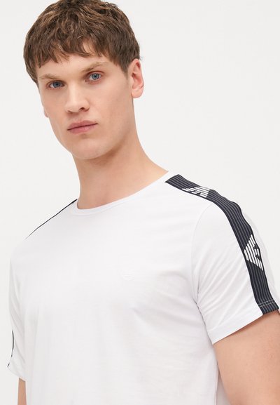 White short-sleeve t-shirt with black stripe detail on shoulders and textured accents, featuring a subtle logo on the chest.