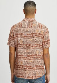 Camisa de manga corta en óxido con patrones geométricos en crema y naranja. Tejido texturizado con collar regular, que presenta un dobladillo recto.
