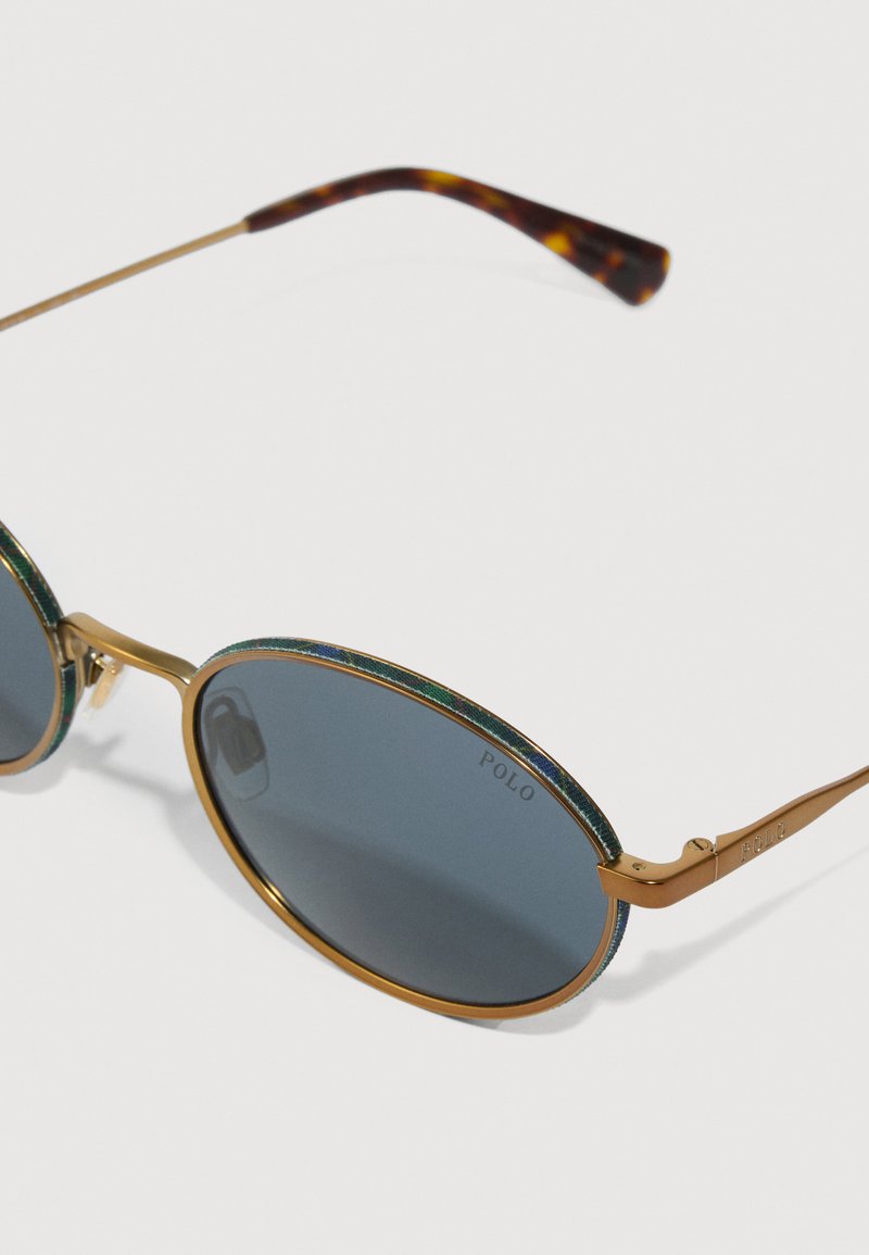 Lunettes de soleil avec une monture dorée, des verres ovales, des accents verts et bleus, et des verres gris foncé. Présentent un logo Polo sur la monture.