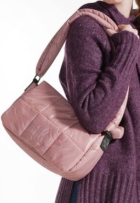 Borsa a spalla trapuntata rosa con superficie liscia, dettaglio del logo, tracolla regolabile e forma rettangolare, abbinata a un maglione viola.