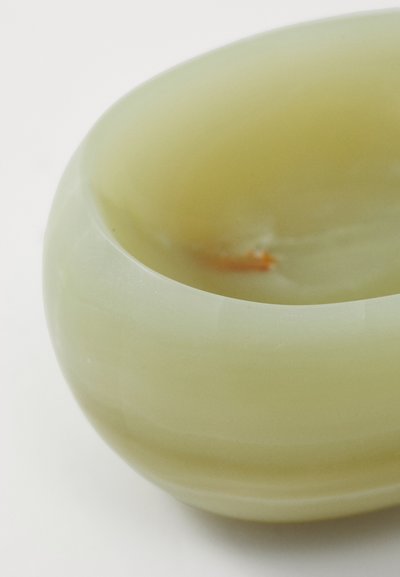 Translucent light green bowl with smooth, rounded shape and a glossy finish. An orange detail is visible inside. Made from stone or resin.