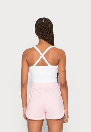 Biały top na ramiączkach z krzyżowanym tyłem, zestawiony z jasnoróżowymi szortami, z elastycznym pasem i miękką fakturą materiału.