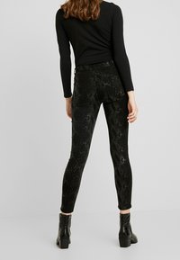 Leggings de imitación de cuero negros con un patrón de piel de serpiente, que presentan un ajuste ceñido y una textura contrastante, combinados con botas hasta el tobillo.