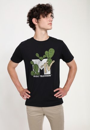 Black cotton t-shirt featuring a cactus-themed graphic with "MTV" in white and beige, set against a textured design. Worn with beige pants.