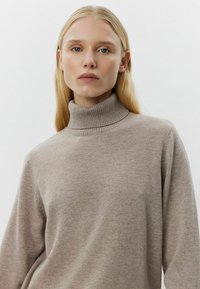 Pulover bej cu guler înalt, confecționat dintr-un material moale. Are mâneci lungi și o croială lejeră, design minimalist.