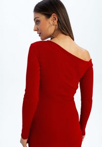 Czerwona, prążkowana sukienka z długim rękawem w stylu off-shoulder. Materiał ma teksturowany wygląd, a sylwetka jest dopasowana.