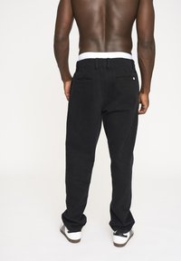 Sorte bukser med en afslappet pasform, der har en hvid elastisk talje og baglomme. Stofudseendet er glat med minimal tekstur.