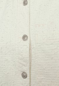 White textured fabric shirt with visible stitching, featuring silver metallic snap buttons and a small chest pocket.