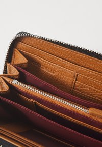 Rudas odinis pinigine su keliais kortelių skyriuose, bordo spalvos audinio akcentai ir sidabrinės užtrauktuko detalės. Strukturizuota odos apdaila.