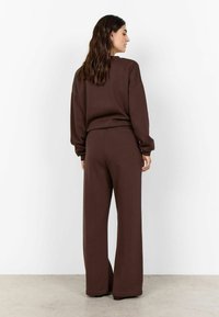 Brun oversized sweatshirt och matchande vida byxor, tillverkade av mjukt tyg. Designen har en avslappnad passform och långa ärmar.