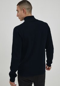 Pulover tricotat bleumarin, cu guler înalt, manșete și tiv cu nervuri. Textură netedă și siluetă ajustată, prezentat din spate.