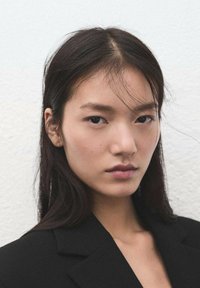 Primer plano de una persona con cabello largo y oscuro, que lleva una chaqueta negra. El fondo es claro. La piel tiene un tono natural con maquillaje mínimo.