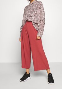 Camisa de manga larga con estampado de leopardo en colores claros; pantalones anchos de canalé en color óxido. Combinada con zapatillas negras con suelas blancas.
