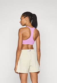 Lilla sports bh med racerback-design; kombinert med lyse beige shorts med elastisk liv og en liten detalj.