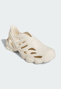 Light beige slip-on shoe with cutout design, textured surface, and rounded toe. Features prominent heel and flexible material.