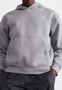Hoodie grigio in cotone misto con tasca frontale, polsini e orlo a coste, e logo Jordan bianco sul petto, abbinato a pantaloni neri.