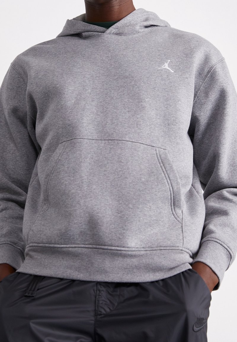 Hoodie grigio in cotone misto con tasca frontale, polsini e orlo a coste, e logo Jordan bianco sul petto, abbinato a pantaloni neri.