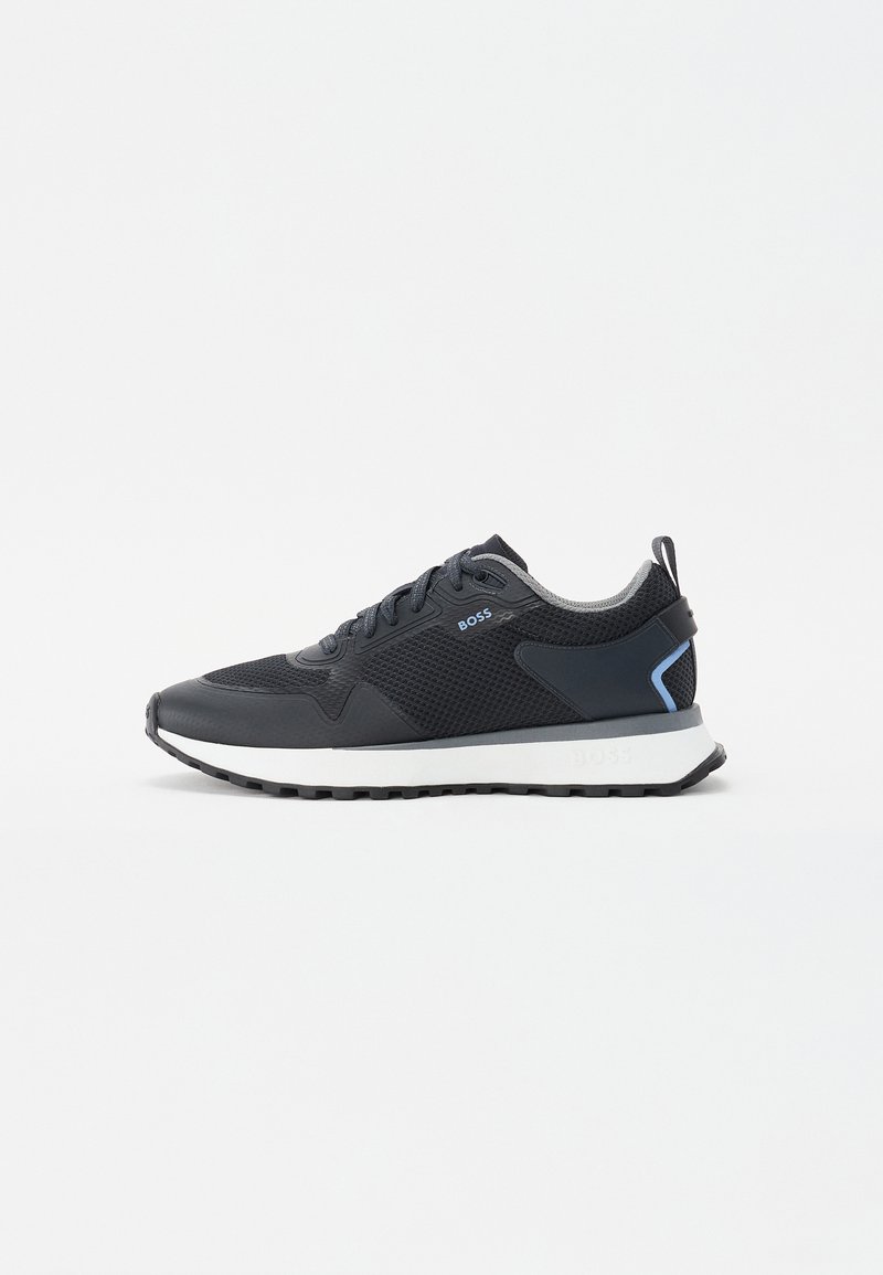 Grijze sportieve schoen met een bovenwerk van mesh, contrasterende donkergrijze neus en hiel, gestructureerde zool en minimalistische blauwe logo-accenten. Lichtgewicht ontwerp.