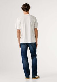 Biele bavlnené tričko s krátkymi rukávmi, doplnené tmavomodrými riflami z denimu. Denný strih; viditeľné švy na rifliach a svetlohnedá obuv.