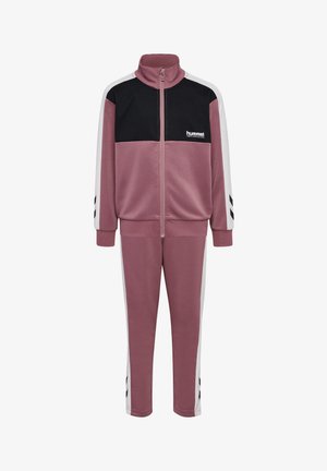 To børn iført matchende sportsdragter i mauve, sort og hvid med lynlåstrøjer og sneakers, står foran en ensartet hvid baggrund.