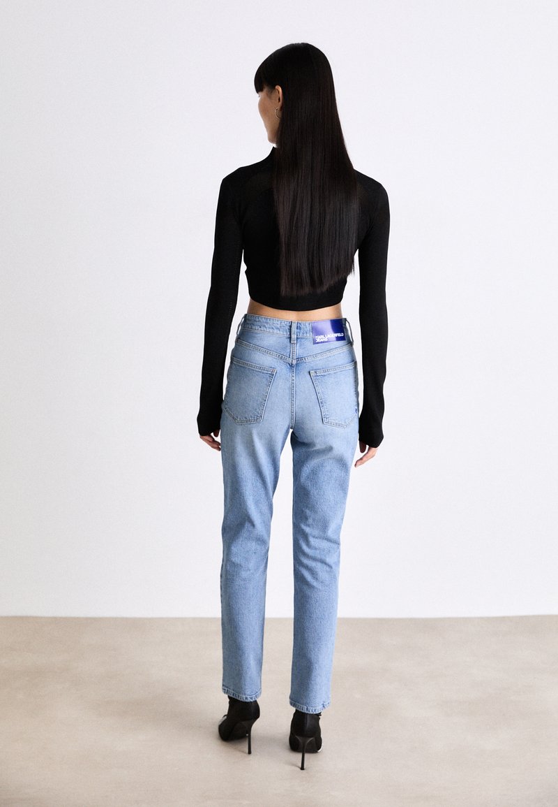 Hoch taillierte, hellblaue Jeans mit geradem Bein und zwei Gesäßtaschen, kombiniert mit einem schwarzen, langärmeligen Crop-Top und schwarzen High Heels.