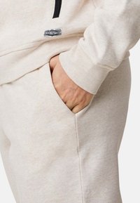 Beige bomullströja med dragkedja och framficka. Har ribbade ärmmuddar och en liten svart etikett på bröstet. Mjuk textur.