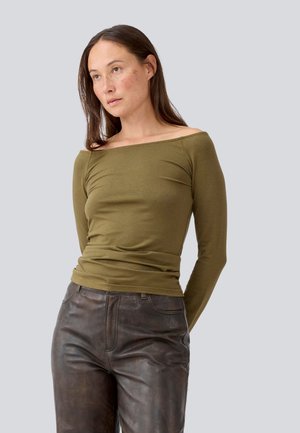 Olivengrønn av-shoulder langermet topp laget av mykt stoff, kombinert med brune skinnbukser. Tettsittende design med glatt tekstur.