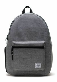 Sac à dos en tissu gris avec un dessus arrondi, il comporte une poche zippée à l'avant, des accents de fermeture éclair noirs et une petite étiquette de marque en bas.