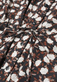 Černá tkanina s bílým květinovým vzorem a hnědými listy, se černými knoflíky a opaskem na zavázání v pase.