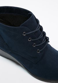 Bottine en daim bleu marine avec six œillets et bout arrondi. Surface texturée avec une finition mate et un petit talon compensé noir.