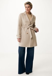 Abrigo de mezcla de lana beige con cinturón en la cintura, cuello con muesca, parte delantera de doble botonadura y botones en tono dorado, combinado con jeans oscuros acampanados.