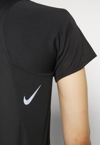 Schwarz athletic T-Shirt mit kurzen Ärmeln, aus strukturiertem Stoff und mit einem weißen Nike Swoosh-Logo auf der linken oberen Seite.