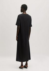 Zwarte katoenen maxi-jurk met korte mouwen, een losse pasvorm, ronde halslijn en een zachte textuur. Eindigt net boven de enkels.