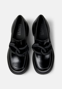 Scarpe in pelle nera con una finitura lucida, caratterizzate da una grande catena nera decorativa e una punta arrotondata su una suola spessa.