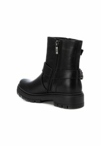 Botas negras hasta el tobillo hechas de cuero suave, con un cierre lateral y una suela de goma gruesa con textura de banda de rodadura. Detalle de correa ajustable.