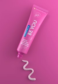 Il dentifricio Curaprox BE YOU in un tubo rosa. Estratto, una linea bianca e ondulata di dentifricio con macchie rosa su uno sfondo rosa.