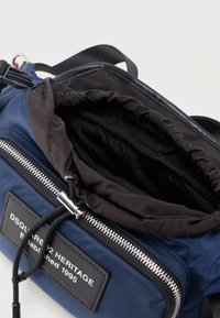 Riñonera DSQUARED2 Heritage azul marino con una bolsa interior de cordón negra parcialmente abierta, cremallera plateada y correa negra ajustable.
