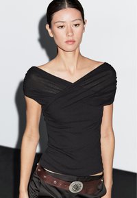 Sort, off-shoulder top med samlede ærmer og tætsiddende design. Sammen med en brun bælte med en rund sølvspænde. Glat stofstruktur.