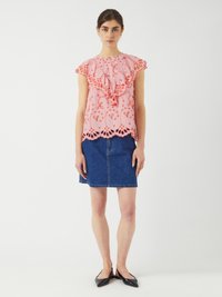 Blusa rosa con maniche a balze e ricami floreali, abbinata a una gonna di jeans. La blusa presenta un orlo scallop e dettagli intricati.